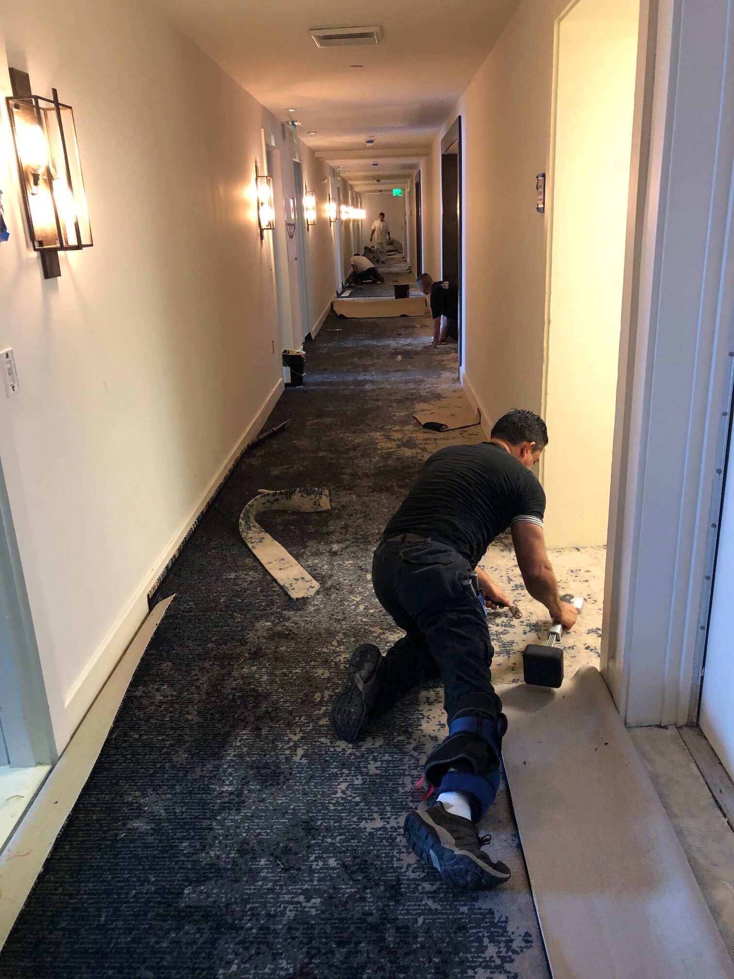 Professional flooring contractors installing a modern dark gray and navy patterned commercial carpet in a long hallway corridor.